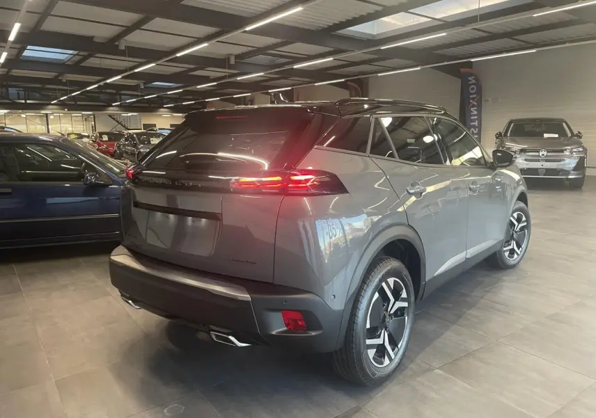 Peugeot 2008 gris métallisé vue 3/4 arrière droit en intérieur avec feux arrière LED allumés.