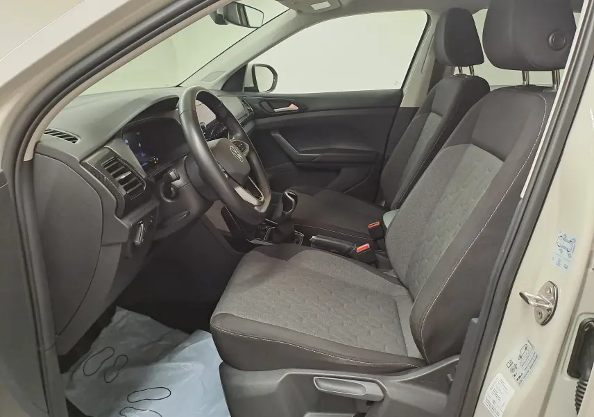 Vue intérieure côté conducteur du Volkswagen T-Cross 2024, sièges tissu gris et tableau de bord moderne.