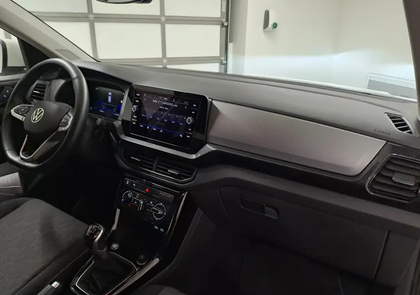 Vue intérieure côté conducteur du tableau de bord et console centrale du Volkswagen T-Cross 2024 avec écran tactile et volant noir.