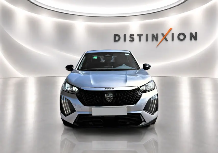 Vue frontale d'un Peugeot 2008 gris 2025 avec calandre noire et feux LED, dans un showroom lumineux.