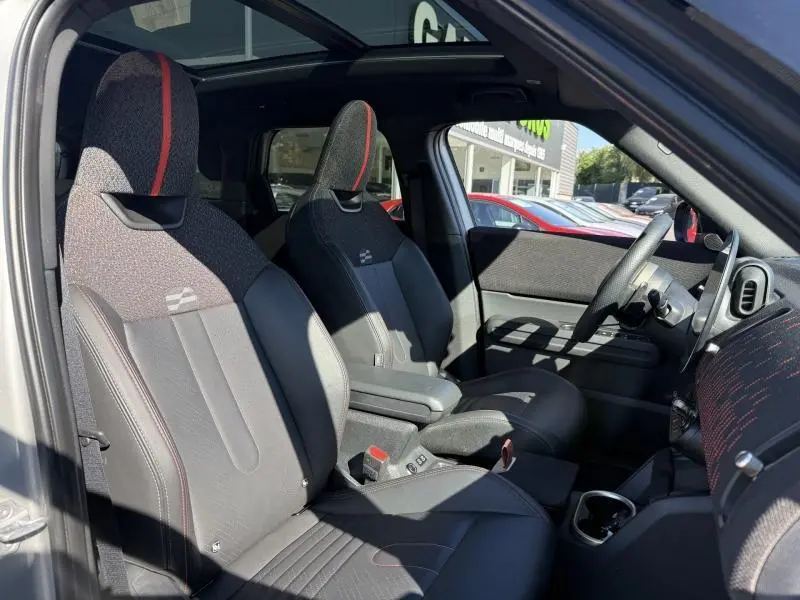 Intérieur avant du MINI Countryman argenté 2025, vue côté gauche montrant sièges sport noirs avec surpiqûres rouges.