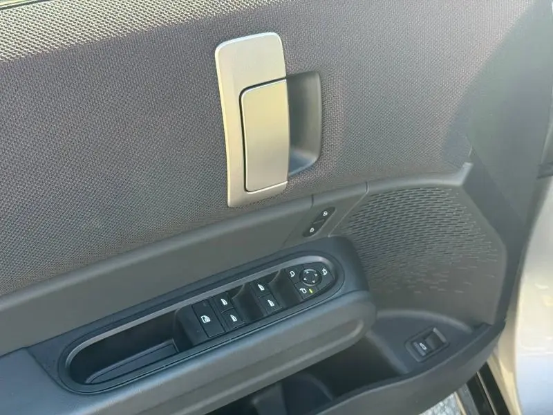 Détail de la porte avant gauche argentée d'une MINI Countryman 2025 avec commandes des vitres et poignée intérieure.