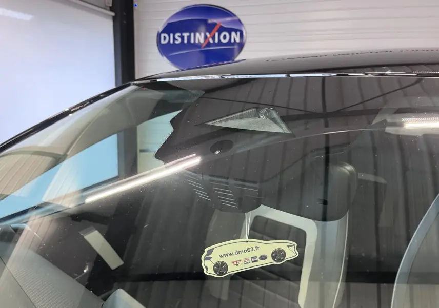 Gros plan sur le pare-brise avant d'une Citroën C4 noire métal, avec caméra et rétroviseur intérieur visibles.