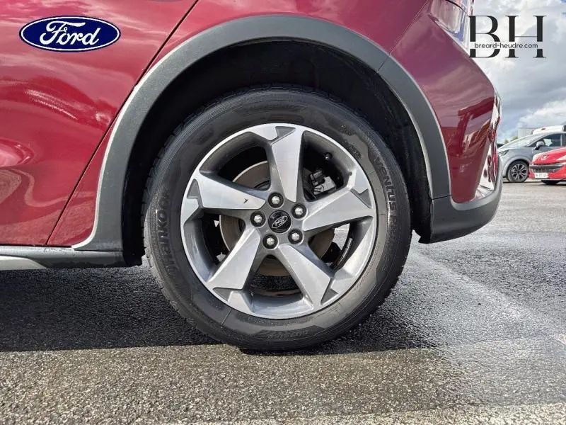 Gros plan sur la roue avant droite d'une Ford Focus 1.0 EcoBoost rouge Premium Candy avec jante alu cinq branches.