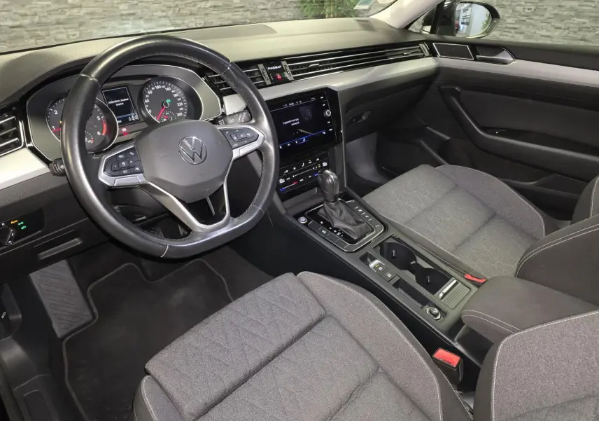 Vue intérieure côté conducteur de la Volkswagen Passat SW 2023, avec tableau de bord noir et sièges tissu gris.
