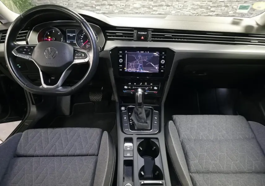 Vue intérieure avant de la Volkswagen Passat SW 2023, tableau de bord noir avec écran tactile et sièges tissu gris.