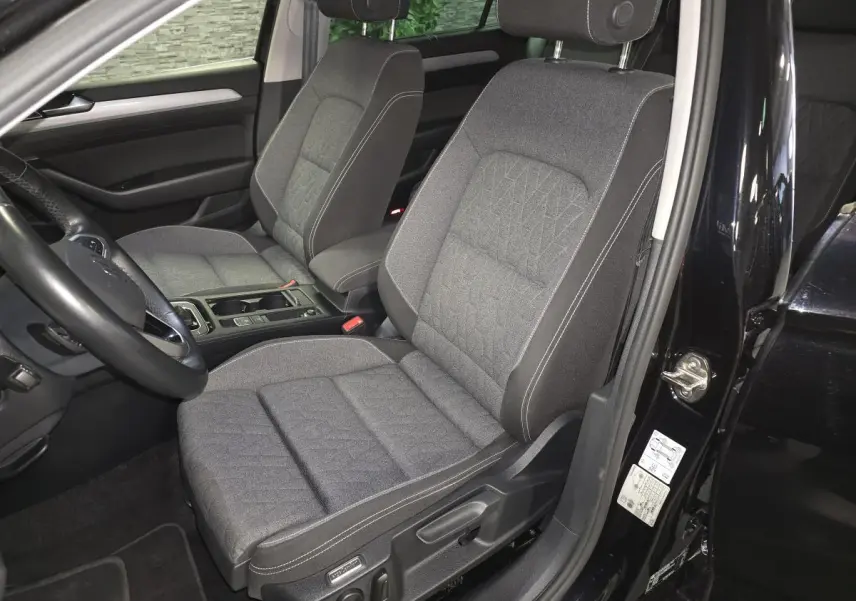 Vue intérieure côté conducteur de la Volkswagen Passat SW 2023 noire, sièges tissu gris avec surpiqûres blanches.