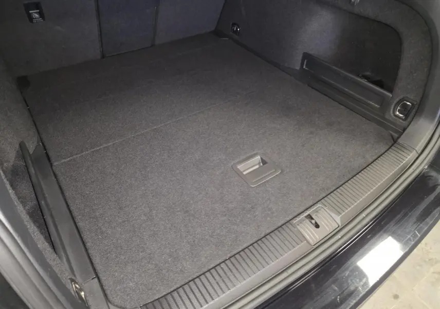 Coffre spacieux de Volkswagen Passat SW noir vu de dessus, avec tapis de sol et anneaux d'arrimage visibles.