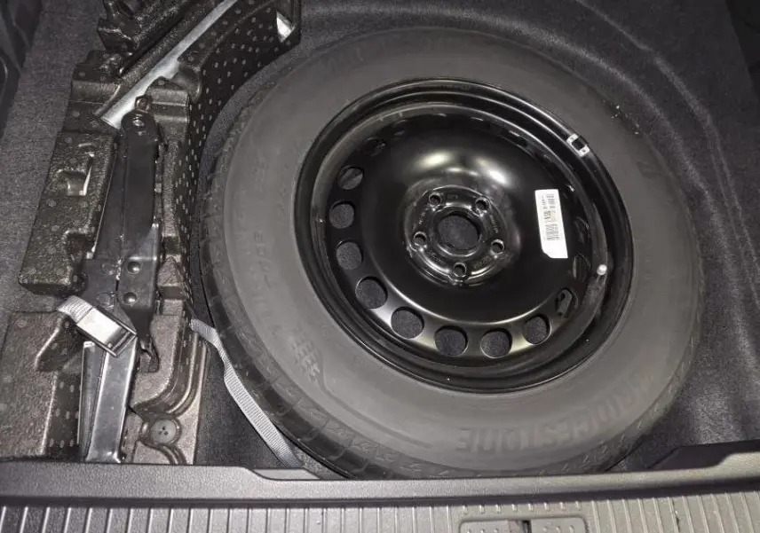 Vue rapprochée de la roue de secours noire en acier dans le coffre d'une Volkswagen Passat SW 2023, avec cric adjacent.