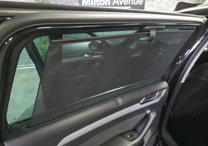 Vue intérieure côté gauche de la porte arrière noire de la Volkswagen Passat SW 2023 avec pare-soleil en filet déployé.