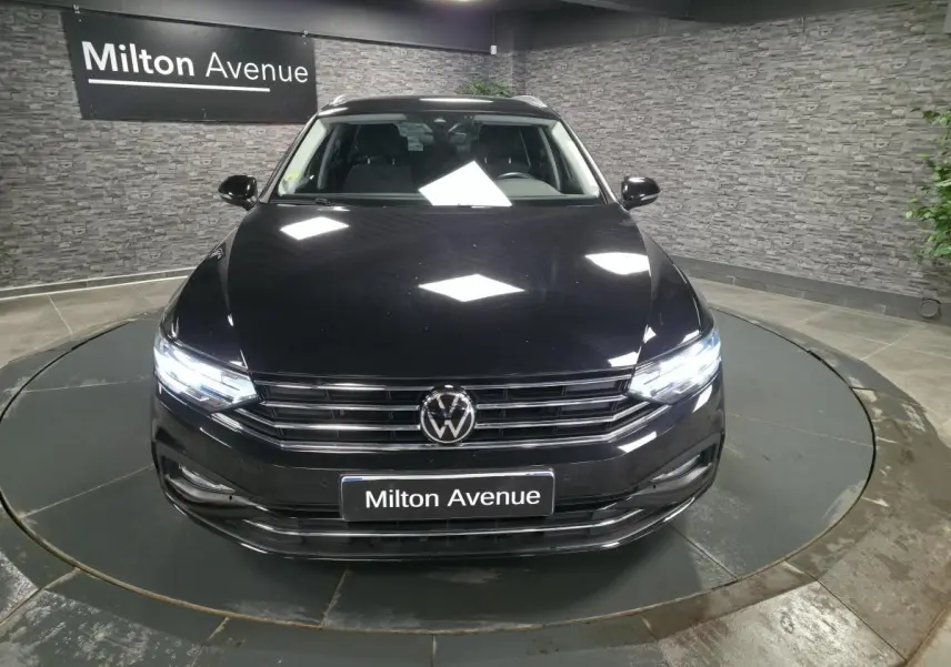Vue avant d'une Volkswagen Passat SW noire avec phares allumés dans un showroom au sol gris.