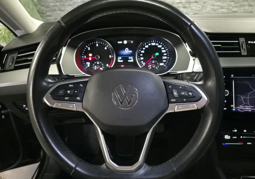 Vue intérieure centrée sur le volant cuir multifonction noir de la Volkswagen Passat avec tableau de bord et écran tactile visibles.