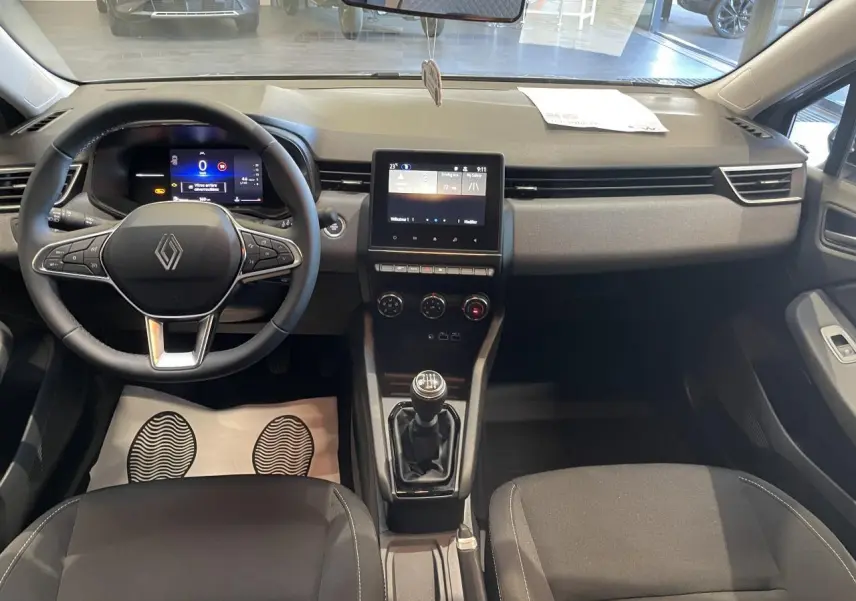 Vue intérieure avant de la Renault Clio 1.5 Blue dCi 2025, tableau de bord gris avec écran tactile et boîte manuelle.