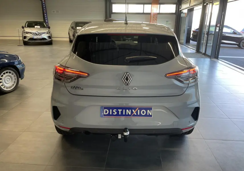 Vue arrière d'une Renault Clio gris Rafale 2025 avec feux LED allumés et attelage visible en intérieur showroom.