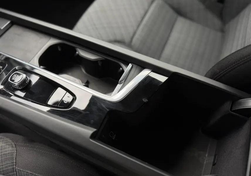 Gros plan sur la console centrale noire brillante de la Volvo S60 2024 avec accoudoir et sièges gris à motifs.