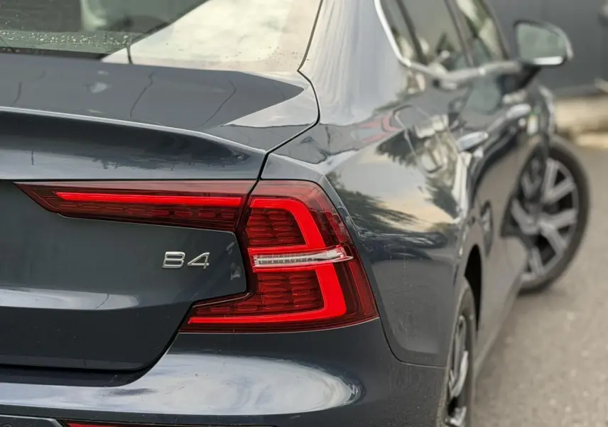 Vue 3/4 arrière droite d'une Volvo S60 B4 gris Denim avec feux arrière LED et jantes alliage 17 pouces.