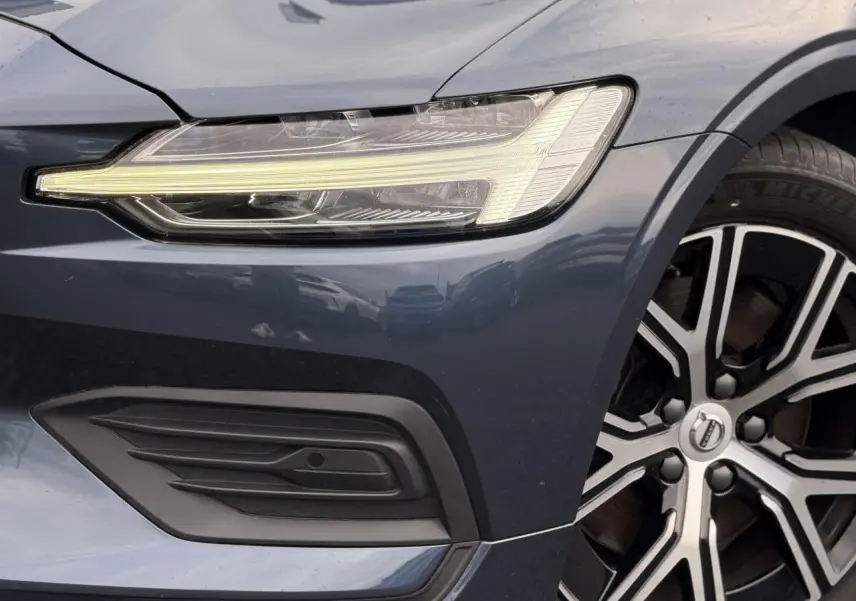 Gros plan sur l'avant droit gris Denim du Volvo S60 2024, mettant en valeur le phare LED et la jante alliage 17 pouces.