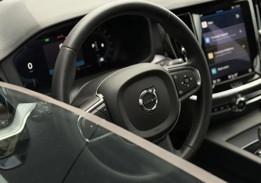 Vue rapprochée du volant noir et du tableau de bord numérique de la Volvo S60 2024, avec écran tactile central visible.