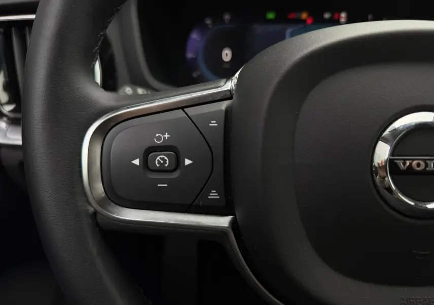 Gros plan sur le volant noir de la Volvo S60 2024 avec commandes intégrées et logo central chromé.