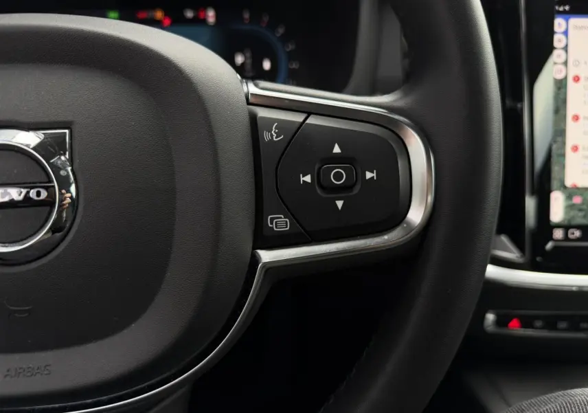 Gros plan sur le côté droit du volant noir de la Volvo S60 2024 avec commandes vocales et multimédia visibles.