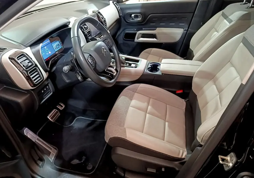 Intérieur clair du Citroën C5 Aircross Hybrid 225, vue côté conducteur avec tableau de bord et sièges beige et gris.