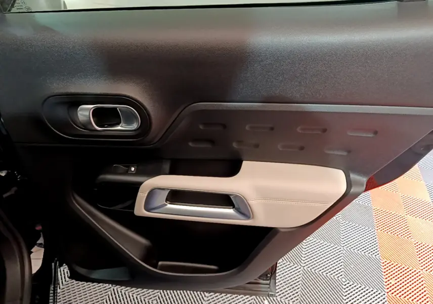 Vue intérieure du panneau de porte côté gauche du Citroën C5 Aircross Hybrid noir, avec insert beige et poignée argentée.