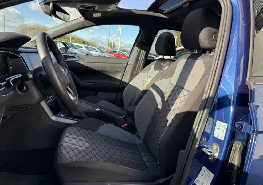 Intérieur côté conducteur du Volkswagen Taigo bleu récif, sièges tissu noir et gris avec motifs géométriques.