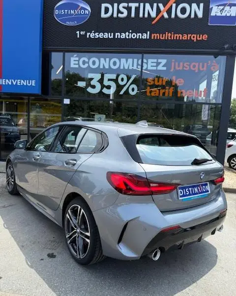 BMW Série 1 118d Edition Sport gris foncé vue 3/4 arrière droit devant un showroom Distinxion.