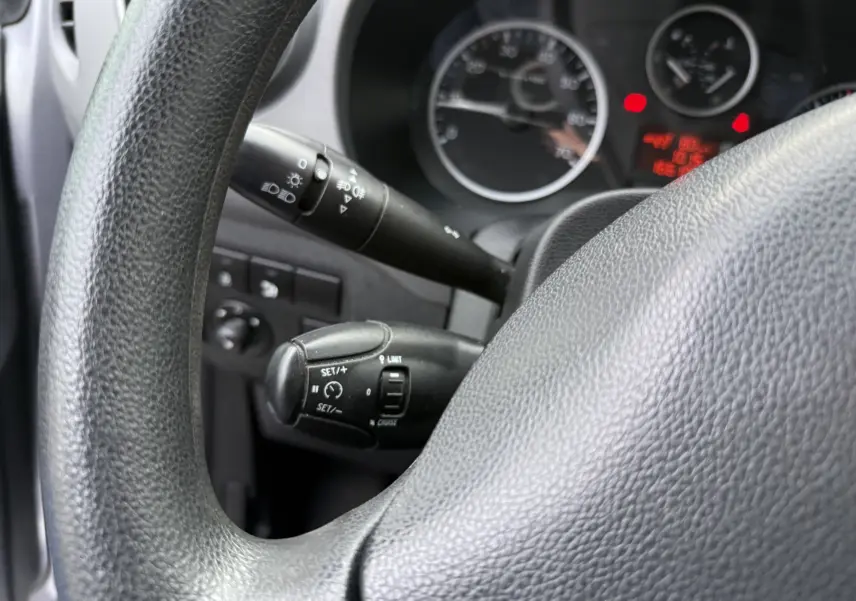 Gros plan sur le volant noir et les commandes de régulateur de vitesse du tableau de bord du Peugeot Partner Tepee gris.