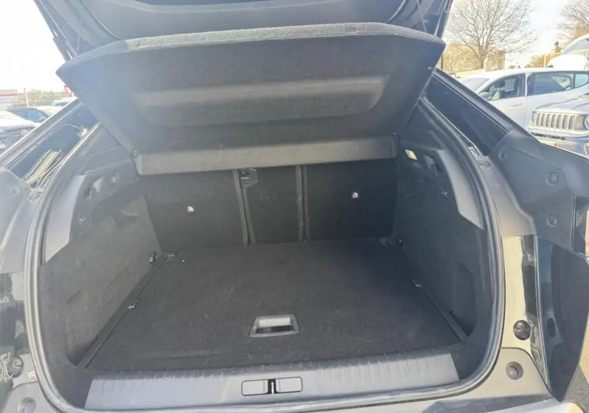 Coffre ouvert vu de l'arrière d'un Peugeot 3008 Hybrid 145 noir, montrant un espace de chargement propre et spacieux.