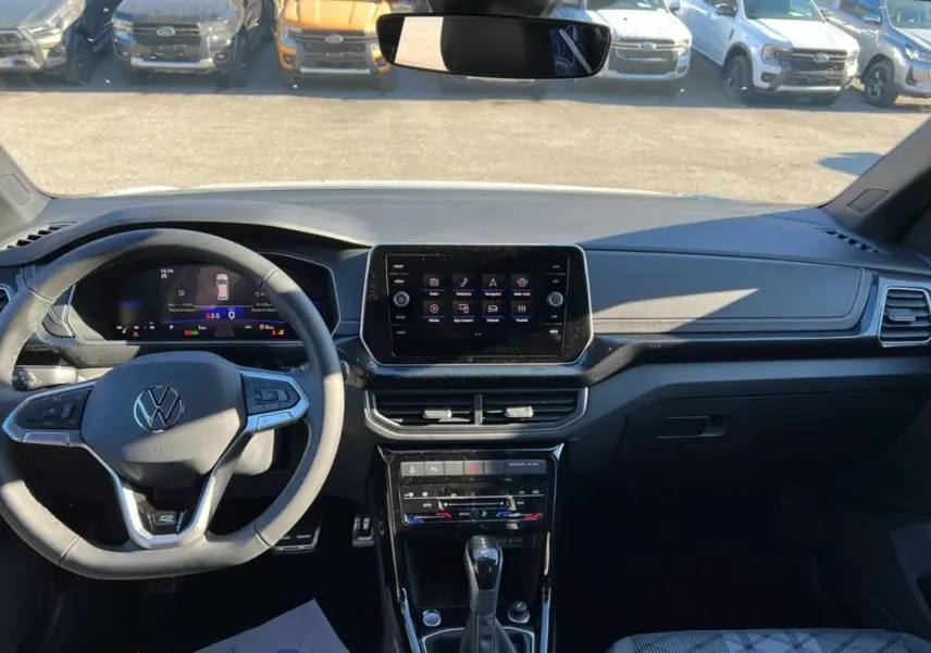 Vue intérieure frontale du tableau de bord noir du Volkswagen T-Cross blanc, avec écran tactile central et volant multifonctions.