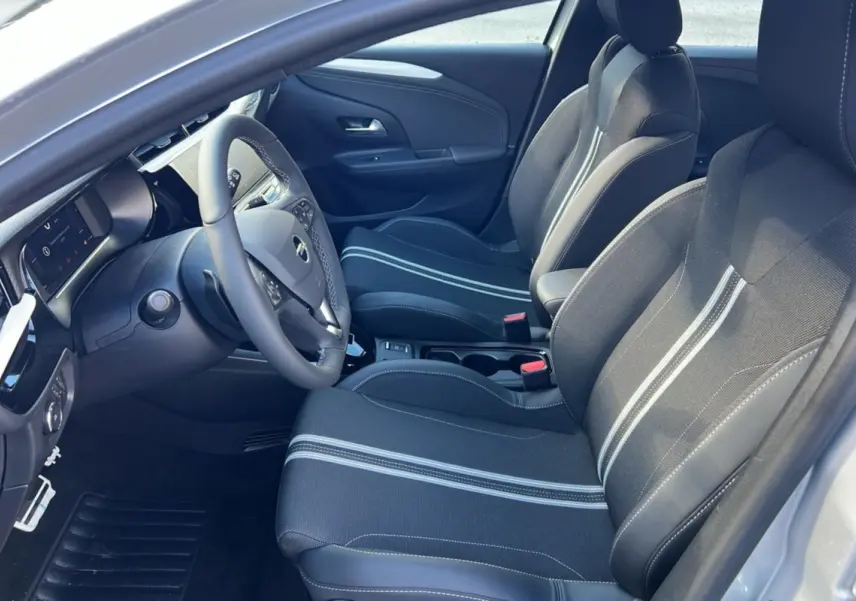 Vue intérieure côté conducteur de l’Opel Corsa Hybrid 110 e-DCT6 gris kristall, sièges tissu avec bandes claires et volant cuir multifonctions.