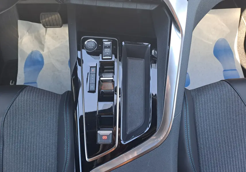 Vue plongeante sur la console centrale noire brillante du Peugeot 3008 2023, avec commandes de boîte auto et rangement.