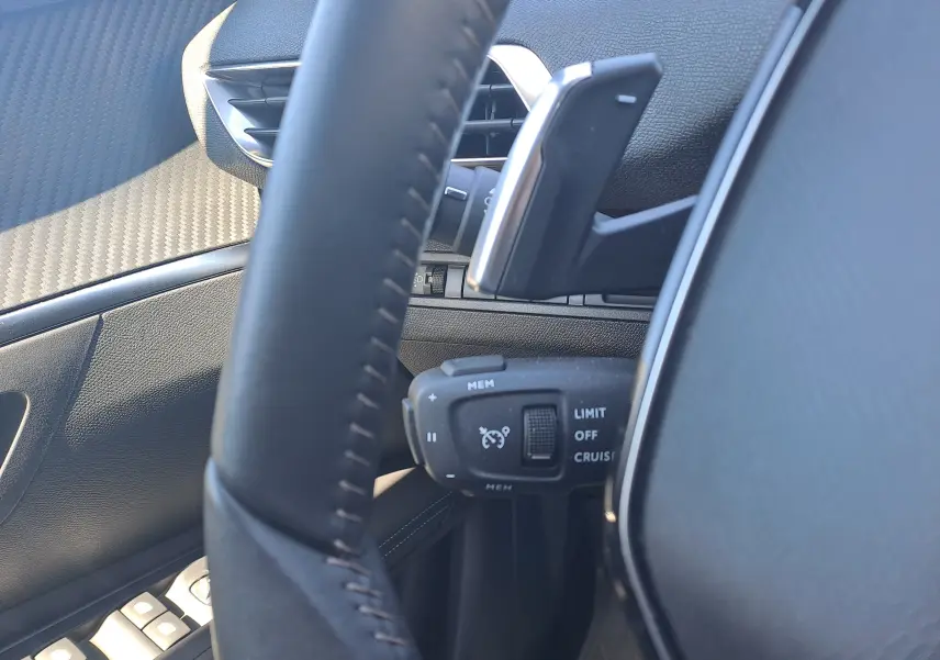 Gros plan sur la commande de régulateur de vitesse derrière le volant noir du Peugeot 3008 2023, intérieur cuir et carbone.