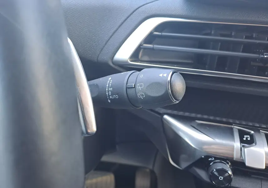 Gros plan sur la commande d’essuie-glace à gauche du volant dans l’habitacle noir du Peugeot 3008 blanc nacré 2023.