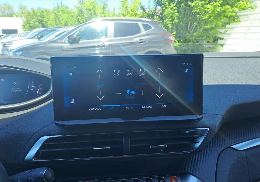 Intérieur du Peugeot 3008 2023 montrant l'écran tactile central de la climatisation, avec tableau de bord noir et extérieur lumineux visible.