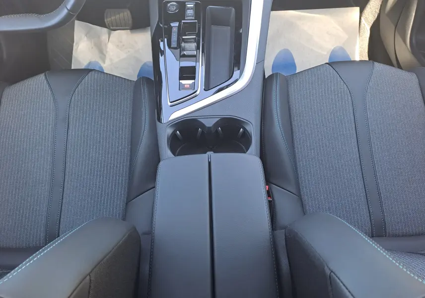 Vue intérieure plongeante sur la console centrale noire et les sièges avant en tissu gris du Peugeot 3008 2023.