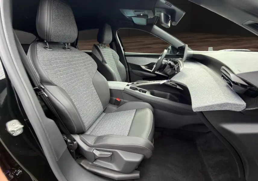 Vue intérieure côté conducteur du Peugeot 3008 noir 2026, sièges tissu et cuir, tableau de bord avec finition tissu gris clair.