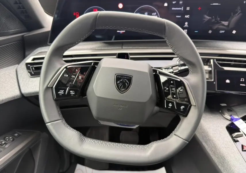 Vue rapprochée du volant cuir gris du Peugeot 3008 2026 avec commandes multifonctions et tableau de bord numérique.