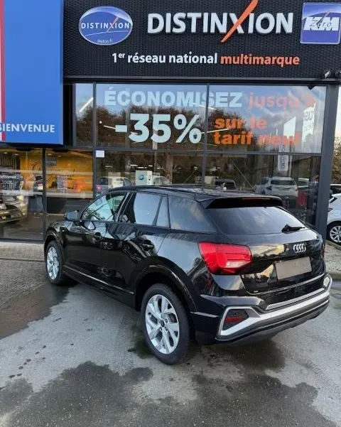 Audi Q2 35 TFSI S Line noir vue 3/4 arrière droit, stationné devant un showroom Distinxion.