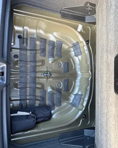 Coffre ouvert vu de dessus d’un Audi Q2 noir 2023, montrant la partie métallique sous la tablette arrière sans roue de secours.