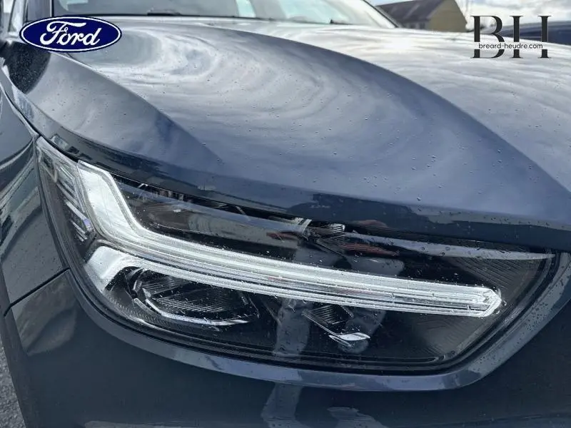 Gros plan sur le phare avant gauche bleu Denim d'un Volvo XC40 T4 Recharge 2021, avec reflets et gouttes d'eau visibles.