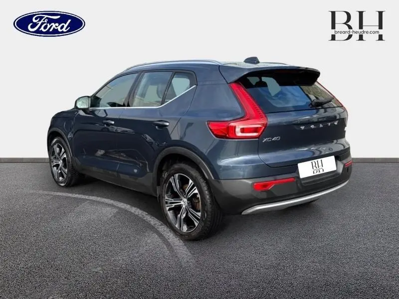 Vue 3/4 arrière droite d'un Volvo XC40 bleu Denim avec feux arrière en L et jantes alliage noires et argentées.