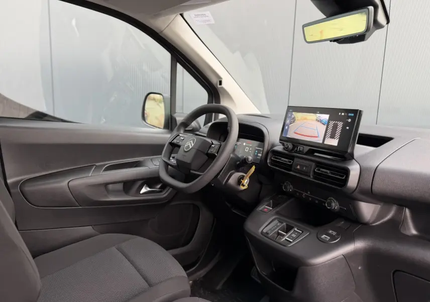 Vue intérieure côté conducteur du Citroën Berlingo blanc, avec tableau de bord numérique et écran tactile affichant la caméra de recul.
