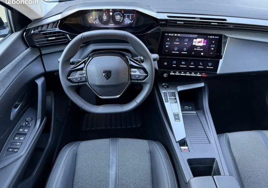 Vue intérieure avant de la Peugeot 308 Hybrid 145 e-DCS6 Allure 2025, tableau de bord et volant cuir noir.