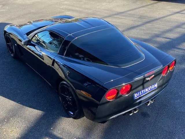 Vue 3/4 arrière d'une Chevrolet Corvette C6 Targa noire de 2005 avec feux ronds et jantes noires brillantes.