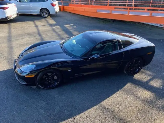Chevrolet Corvette C6 Targa noire vue de 3/4 avant droit, avec jantes noires et toit amovible sous lumière naturelle.