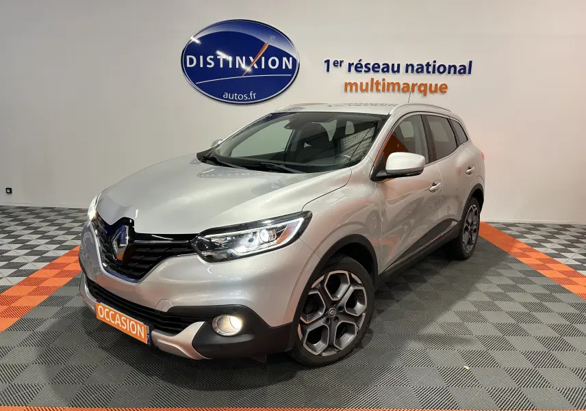 Renault Kadjar gris en 3/4 avant droit, phares et antibrouillards allumés, jantes alliage distinctives visibles.