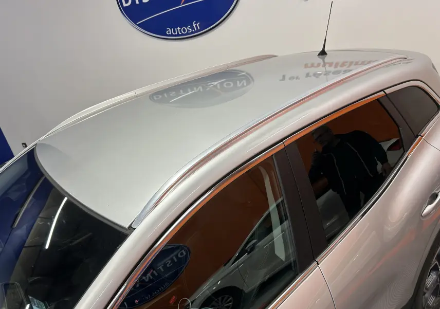 Vue en plongée du côté gauche d'un Renault Kadjar gris métallisé, avec toit et vitres teintées visibles en intérieur showroom.