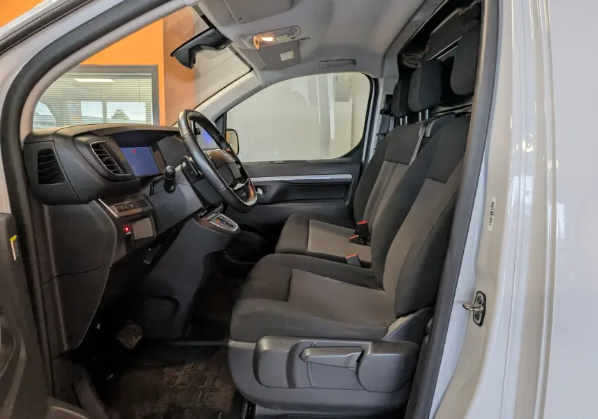 Vue intérieure côté conducteur d'un Opel Vivaro Fourgon blanc 2024, sièges tissu gris et tableau de bord moderne.